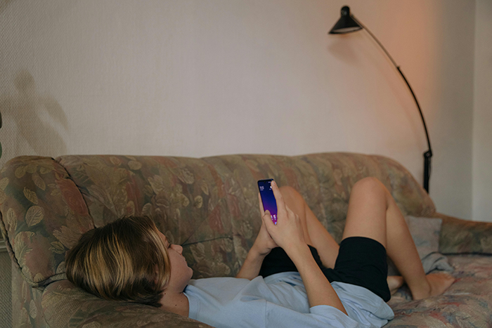 Person relaxing on a sofa, holding a phone, representing anxiety relief in a cozy home setting.