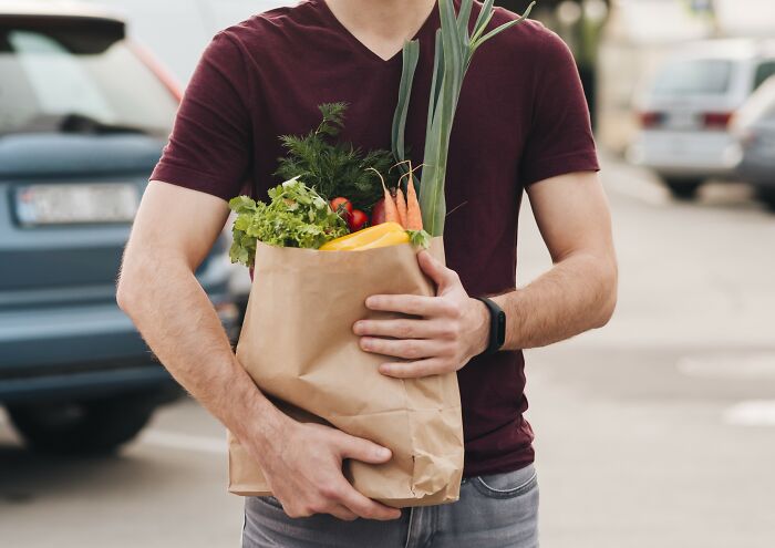 Man holding a paper bag of groceries including carrots and greens, highlighting differences in dating experiences with men.
