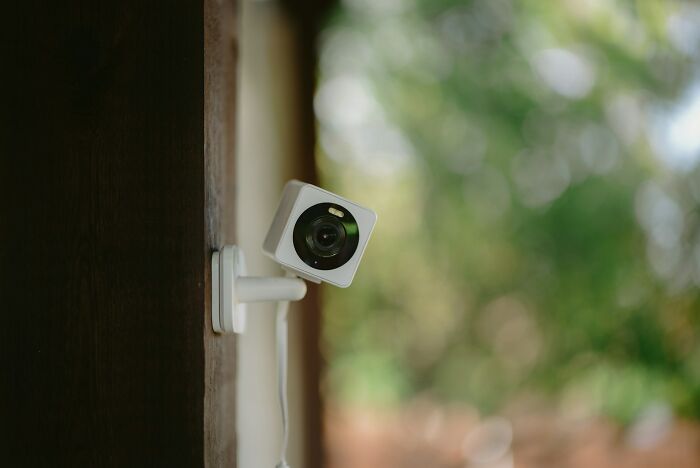 A modern security camera mounted on a wooden wall, capturing outdoor surroundings.