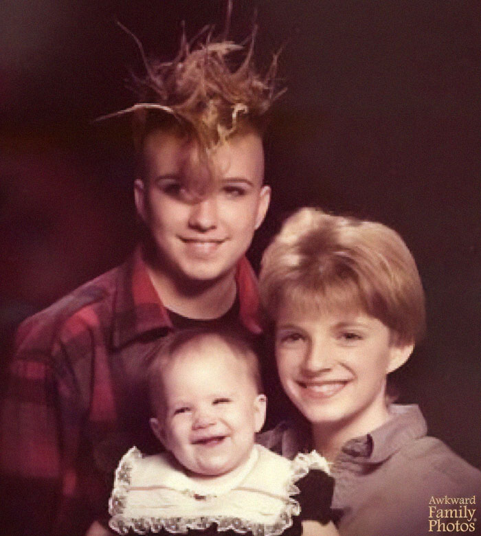 Awkward family photo of three smiling members, featuring unique hairstyles and an infant in a lacy outfit.