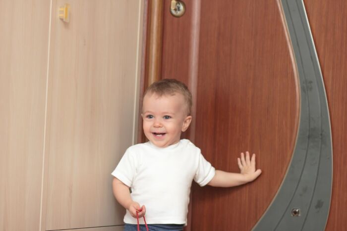 Child smiling playfully by a wooden door, showcasing true comedic charm.