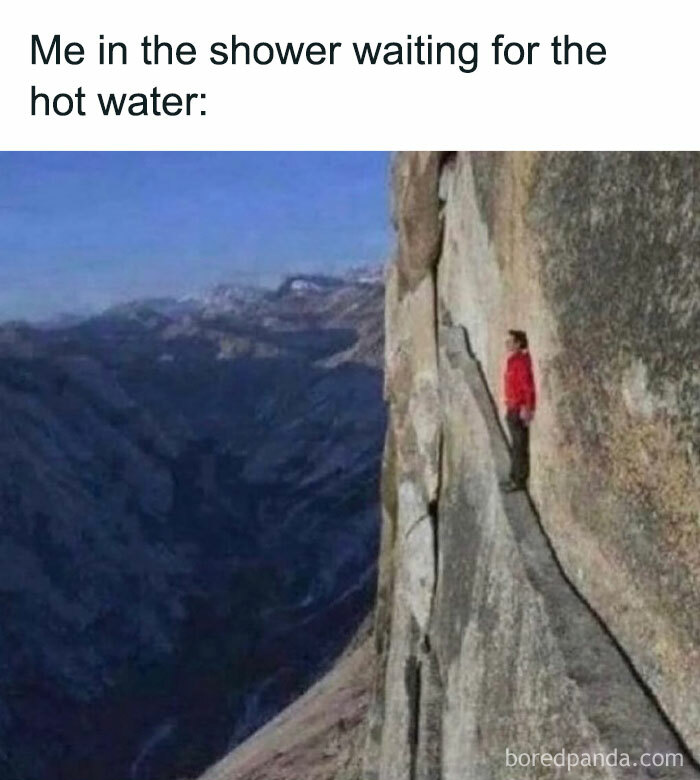 Man in a red jacket standing on a narrow cliff ledge, humorously depicting the wait for hot shower water.