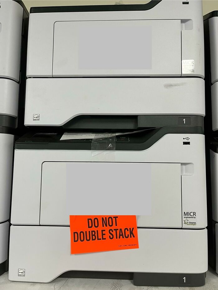 Printers are double-stacked despite sign warning not to, showcasing a confident yet incorrect decision.