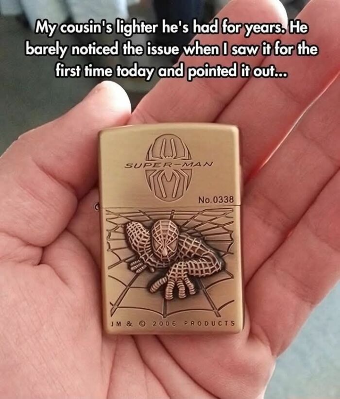 Person holding a lighter with a "Super-Man" engraving, featuring a web-slinging figure; a confidently incorrect design.