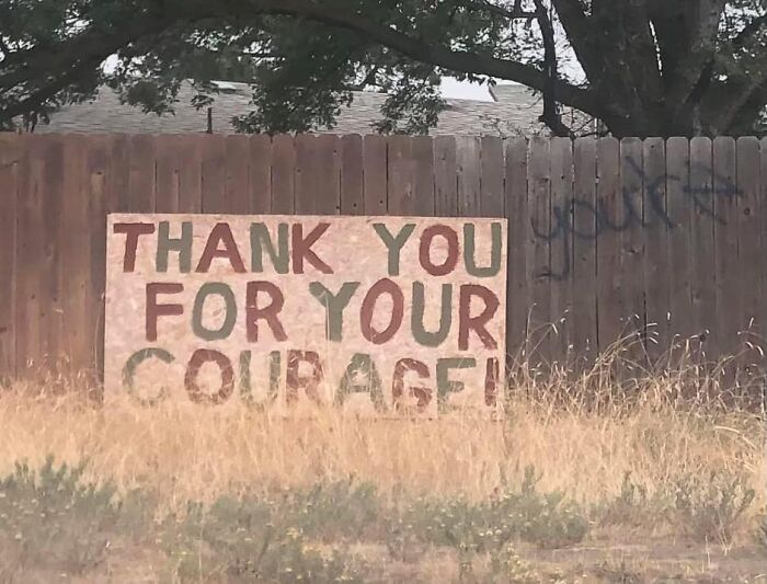 Sign on a fence reads "THANK YOU FOR YOUR COURAGE" with a humorous incorrect graffiti spelling of "You're."