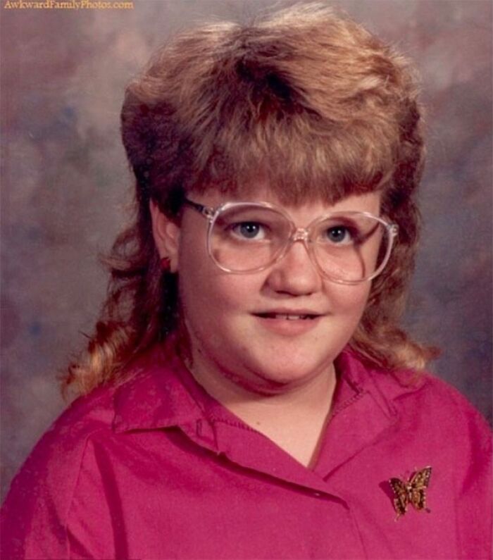 Child with retro hairstyle, large glasses, and a pink shirt featuring a butterfly pin.