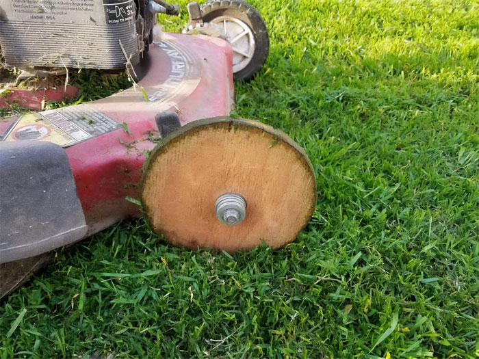 Lawnmower repaired with makeshift wooden wheel, showing a failed repair attempt on green grass.
