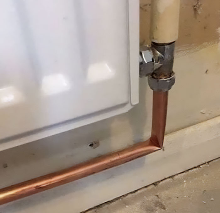 Bent copper pipe connected to a radiator, displaying a failed repair attempt.