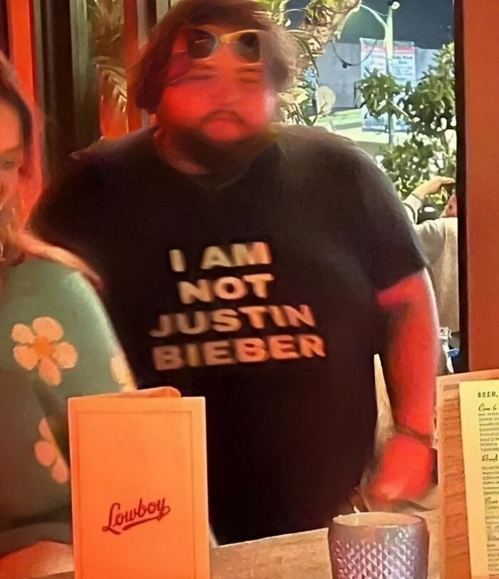 Hombre con camiseta divertida y ridícula que dice no ser Justin Bieber en un ambiente público casual.