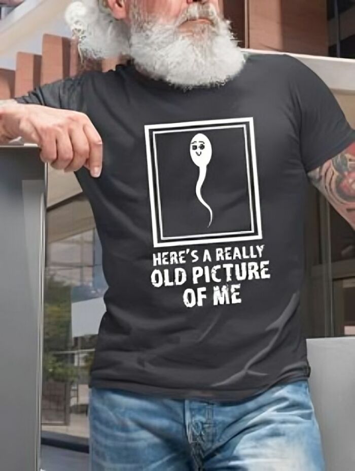 Hombre con barba blanca usando camiseta divertida con diseño ridículo y texto en inglés, en ambiente urbano moderno.