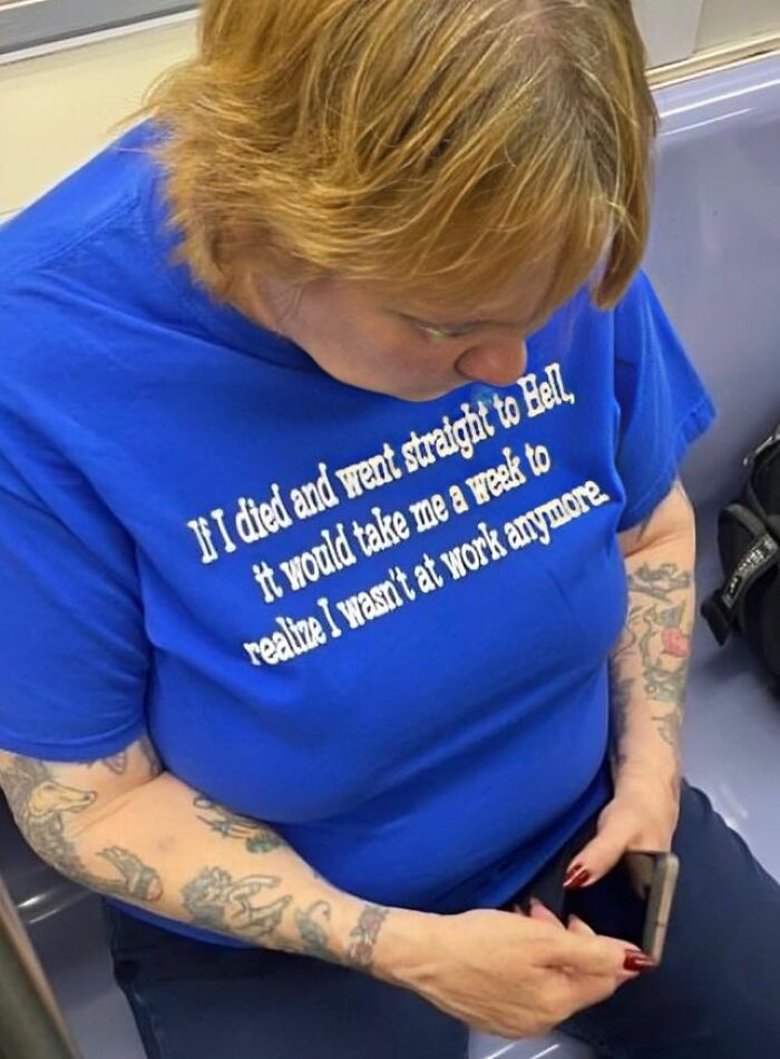 Mujer con camisetas divertidas y ridículas en camiseta azul con texto en inglés, sentada y mirando su celular en transporte público.