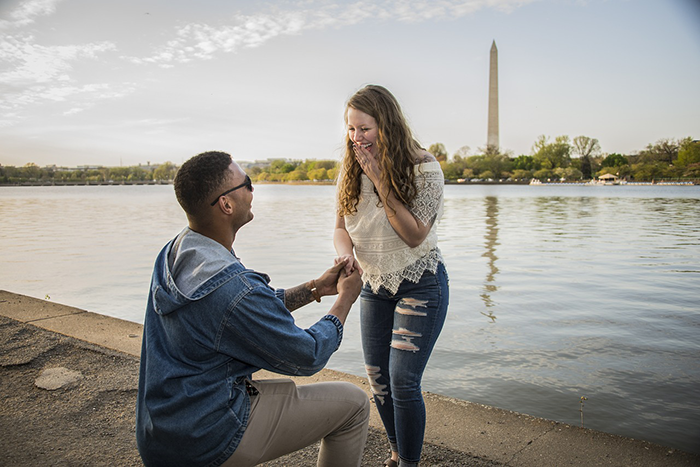 Man proposing to woman by a waterfront, facing inheritance debate over biological kids. Washington Monument in the background.