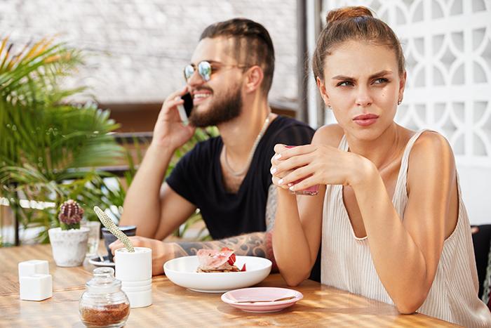 Woman looking upset holding cup, man on phone; tension over family assets and biological kids.