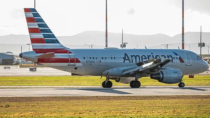 Airlines worker delivers speech amid delay; airplane on runway with mountains in background.