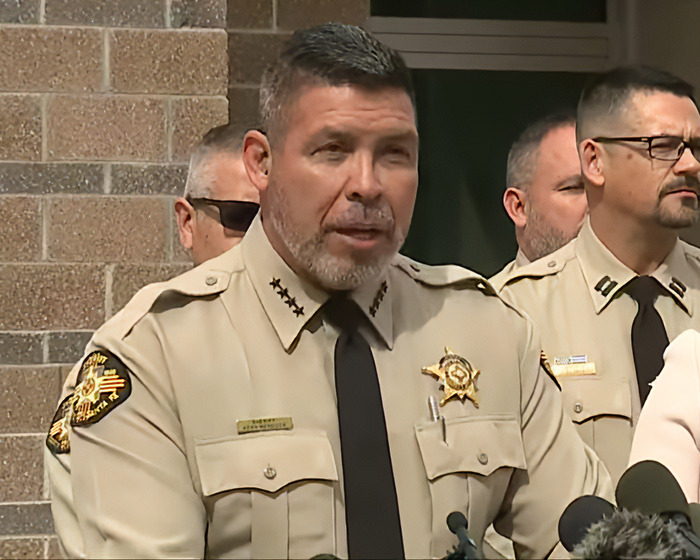 Sheriff in uniform addressing media about Gene Hackman's notes at a press conference outdoors.
