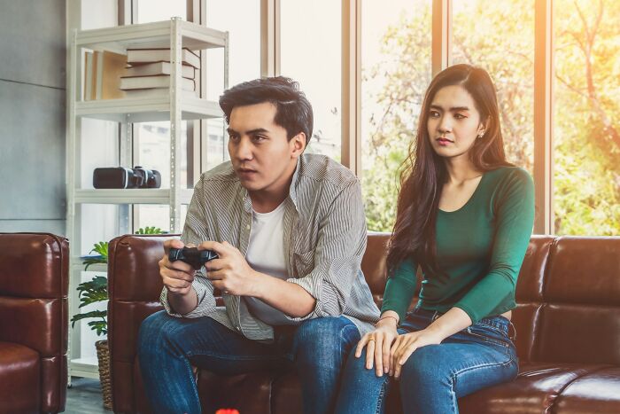 Man focused on video game while woman looks frustrated, highlighting relationship dynamics.