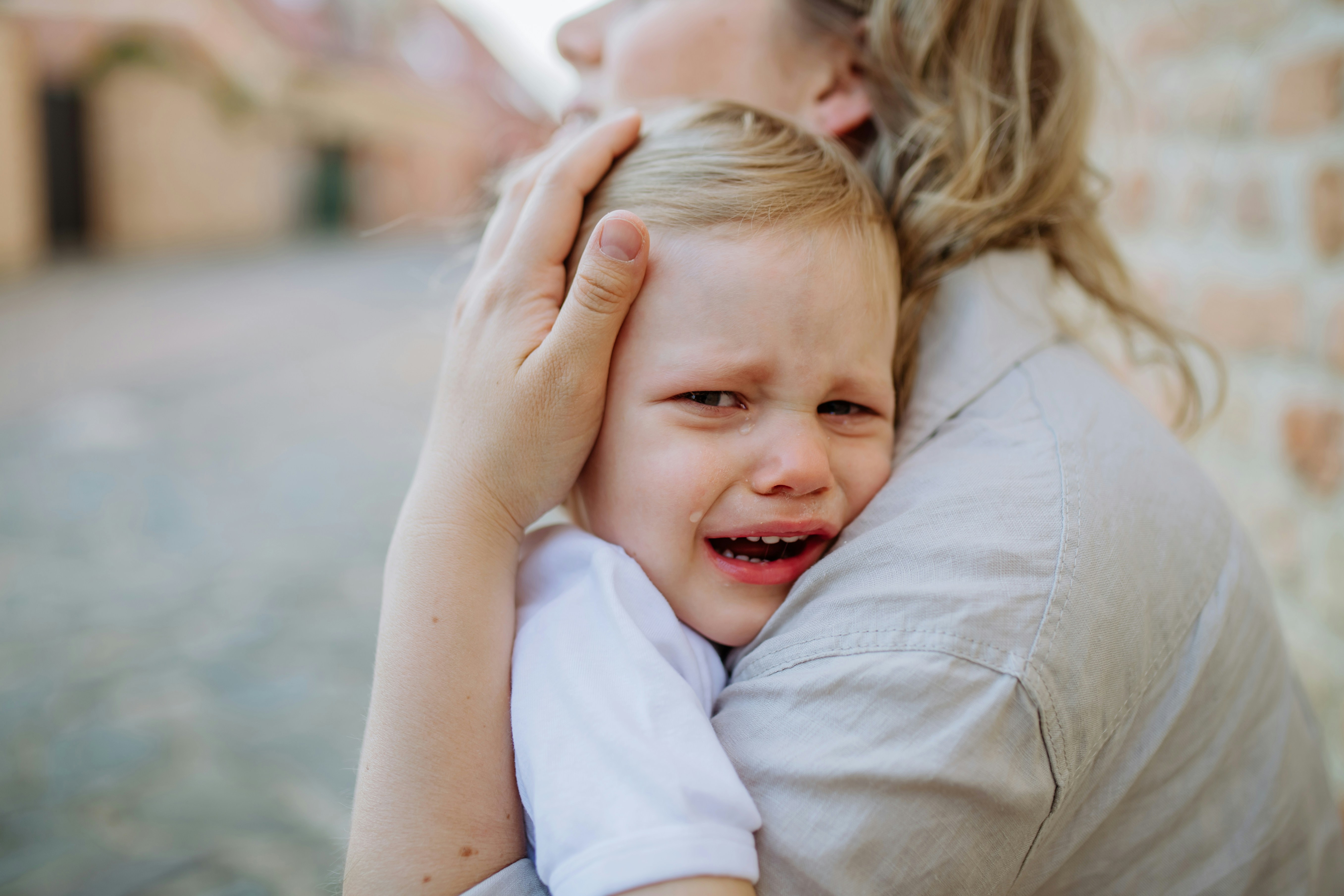 A crying child being comforted by a caregiver outdoors, related to child services.