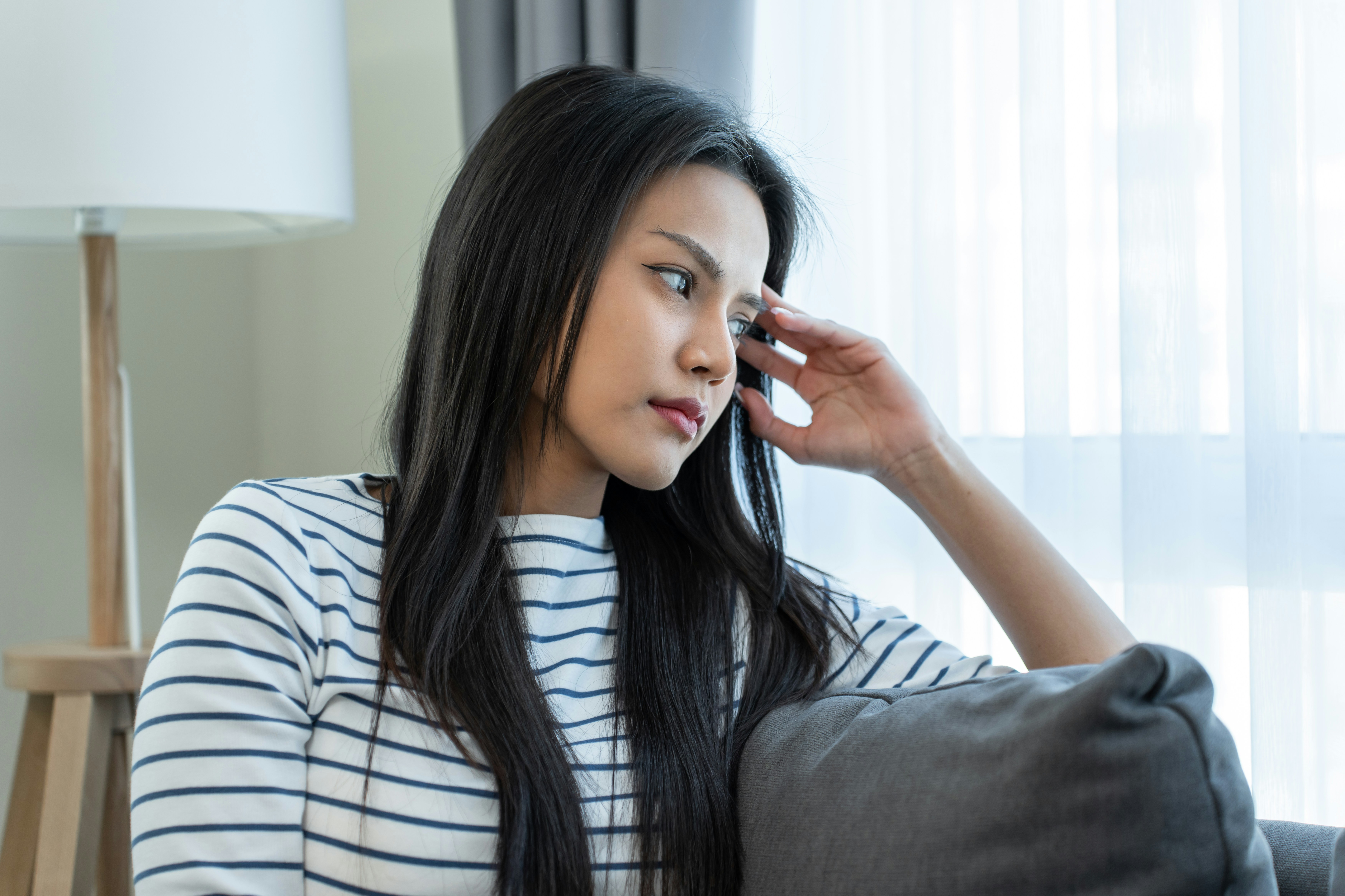 Pensive woman sitting on a couch, reflecting on fianc&eacute;&rsquo;s affair revelation.