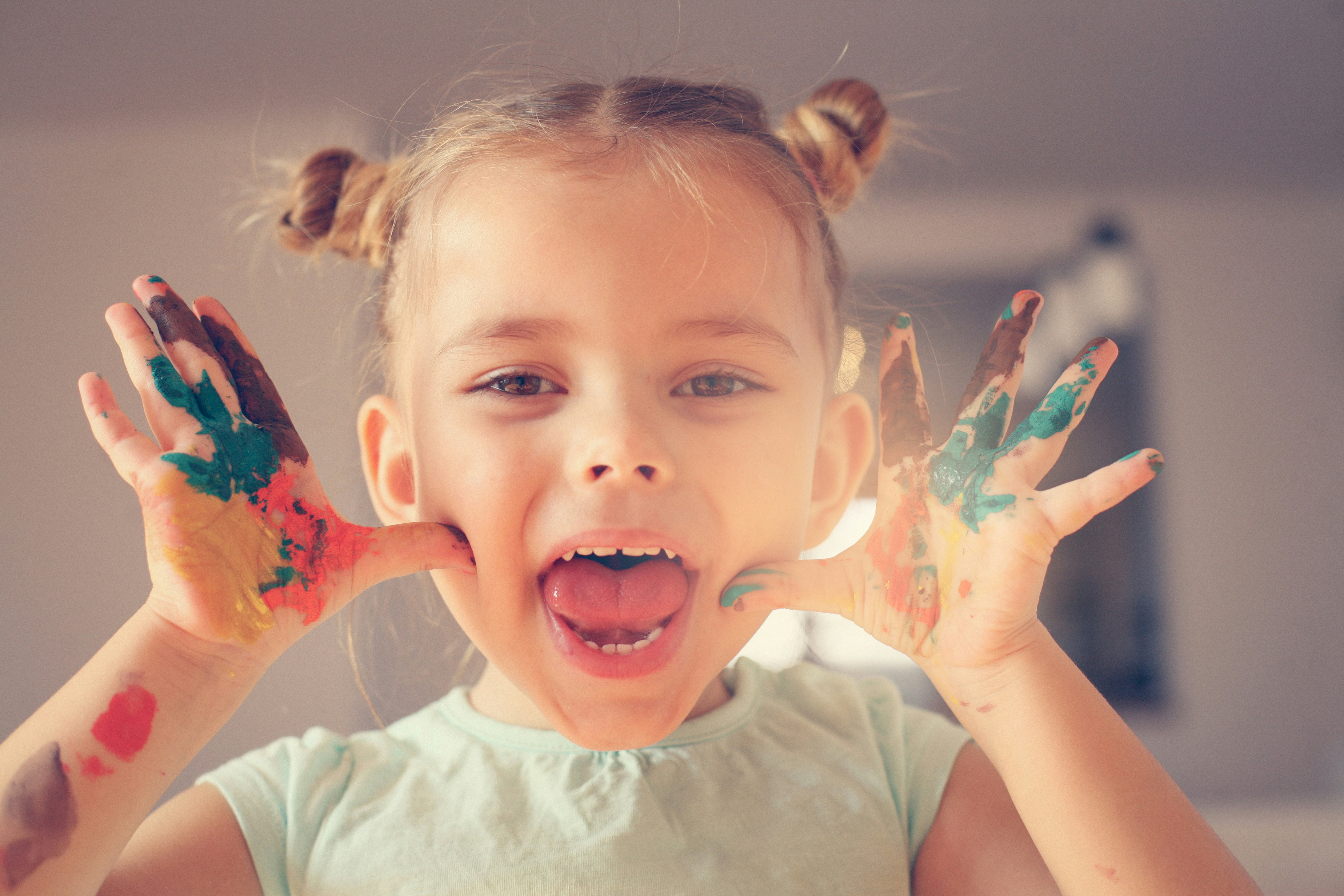 Child with colorful painted hands, smiling playfully; expensive phone case context.