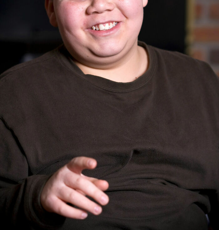 Child smiling in a dark shirt, gesturing toward the camera, symbolizing unseen trauma.