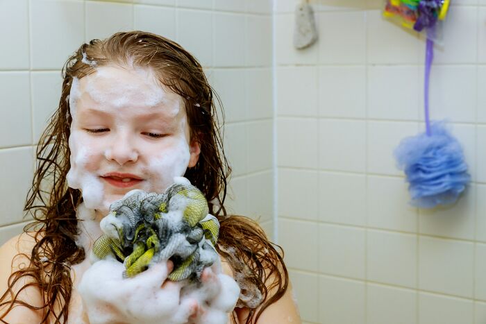 Child covered in soap, holding a foamy toy in the bathtub; a humorous mom sanity hack moment.