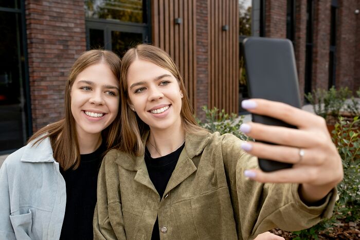 Two women confidently smiling and taking a selfie outside.