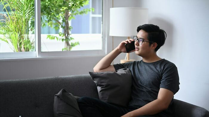 Man in glasses on a couch, talking on phone, with greenery outside window; concept of finding and exploiting loopholes.