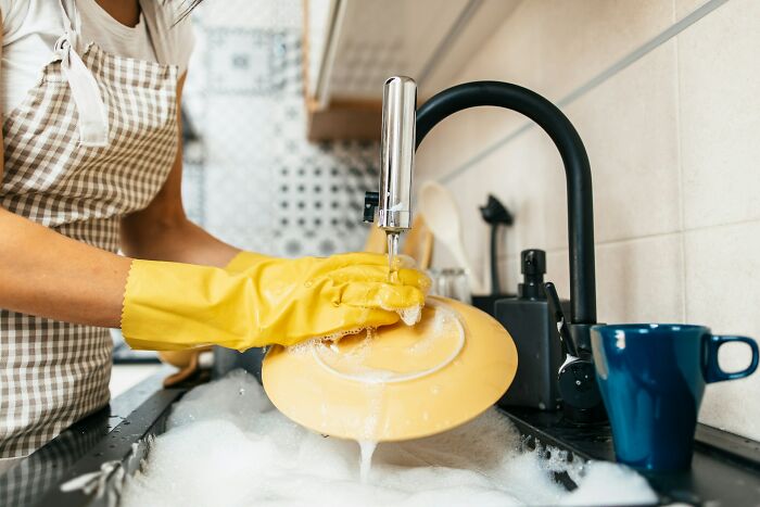 Person wearing gloves washing dishes, illustrating unyielding cleaning rules.