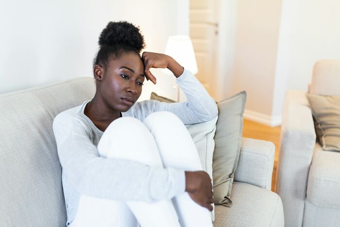 Woman sitting on a sofa, looking pensive and thoughtful.