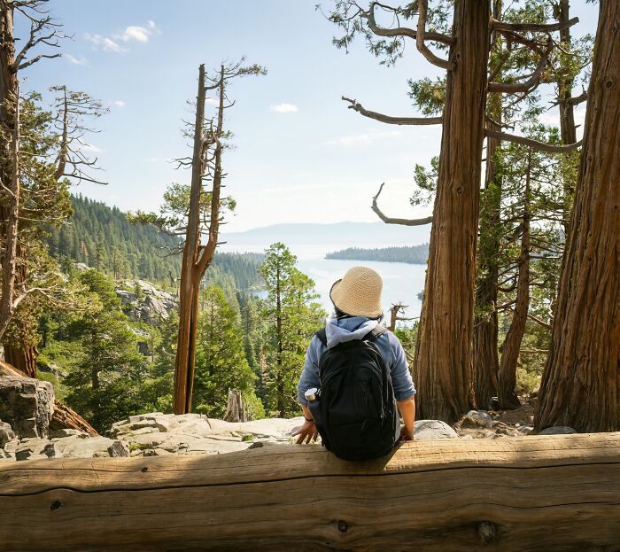 Traveler with backpack and sunhat enjoying scenic island view; trees and water visible in the background.