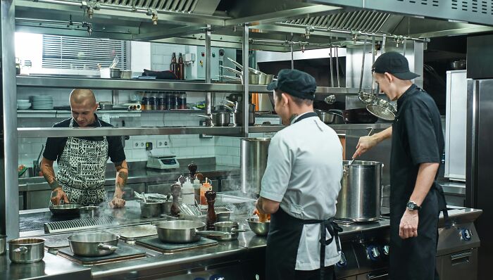 Chefs in a busy chain restaurant kitchen prepare meals, showcasing behind-the-scenes practices.
