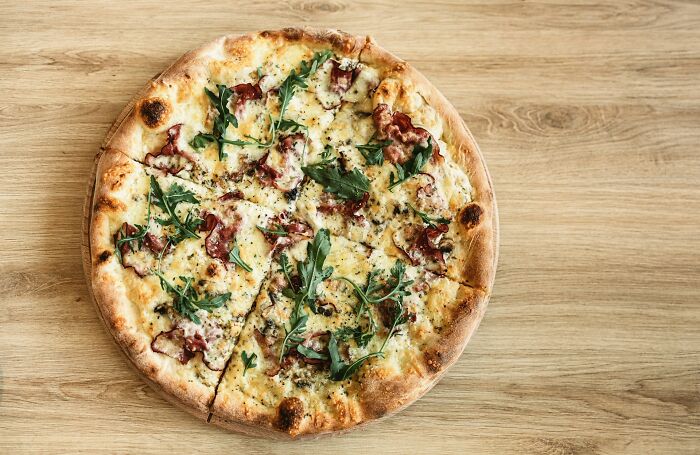 Pizza with arugula and prosciutto on a wooden table, showcasing a delicious food loophole for premium toppings.