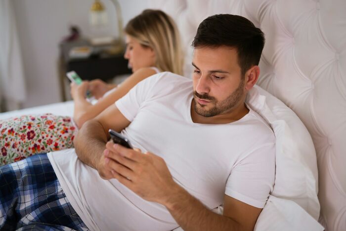 Couple in bed, both focused on their phones, highlighting relationship issues.