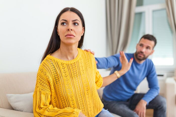 A woman in a yellow sweater appears upset as a man in a blue shirt gestures apologetically, illustrating relationship issues.