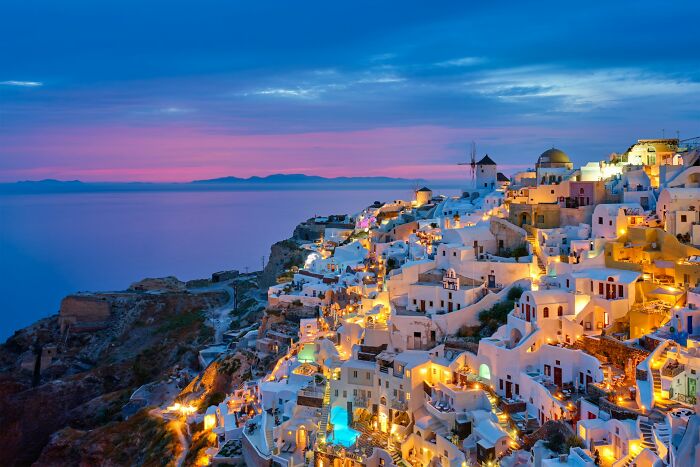 Sunset view of Santorini, Greece, with illuminated buildings, highlighting a luxurious island atmosphere.