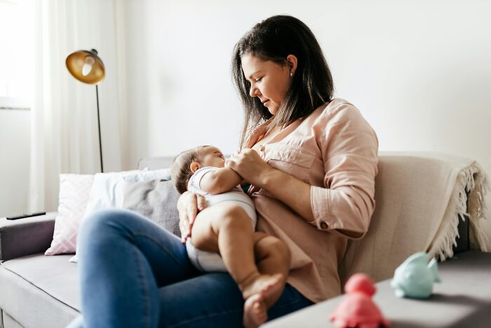 Mother breastfeeding her baby on a couch in a cozy living room showing a super normal thing in the country.