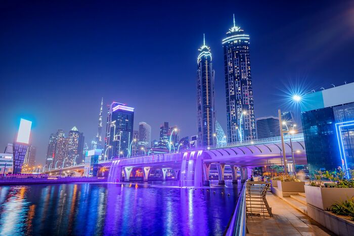 Night view of a cityscape with illuminated skyscrapers by the water, highlighting urban wealth and luxury.