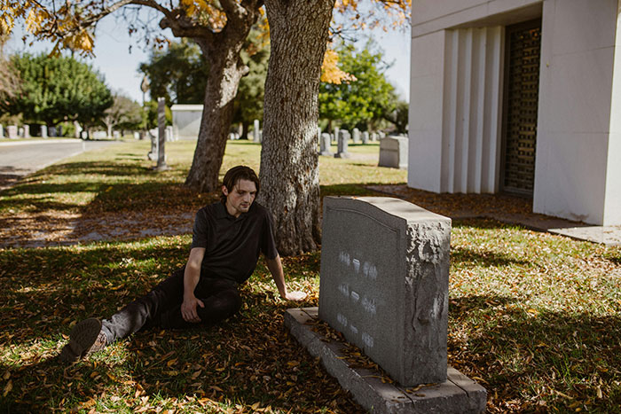 Young man grieving beside a grave in a peaceful cemetery setting. Young man grieving beside a grave in a peaceful cemetery setting.