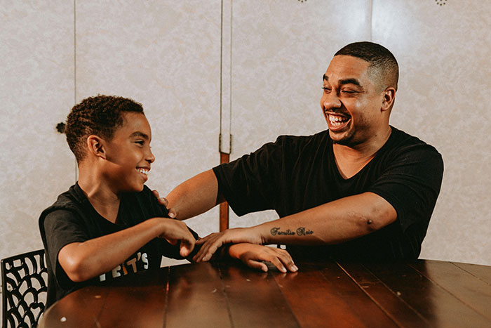 Man and younger brother laughing together at a wooden table. Man and younger brother laughing together at a wooden table.