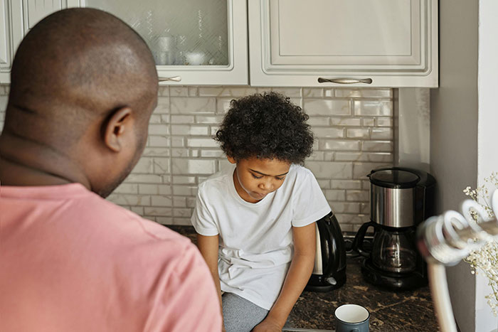 Man and grieving boy talk in kitchen, a kettle and mug on the counter. Man and grieving boy talk in kitchen, a kettle and mug on the counter.