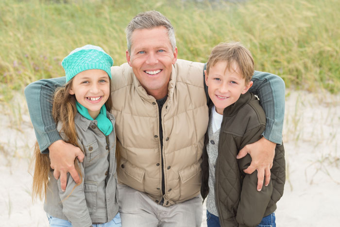 Smiling man with two children, representing a wholesome parent at the beach.