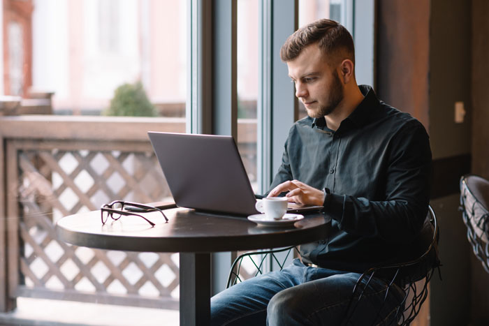 Man at a cafe working on a laptop, unaware of viral Reddit mod's double life.