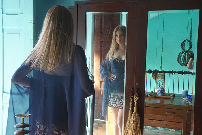 Woman in a blue dress looks at her reflection in a mirror.