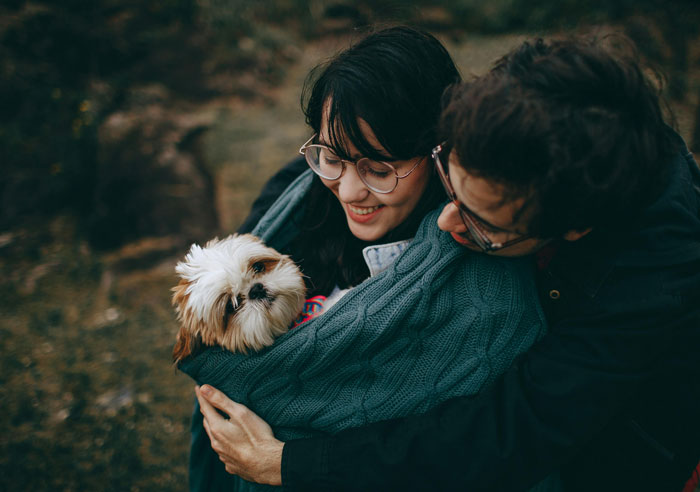 Couple with a small dog wrapped in a green blanket, outdoors.