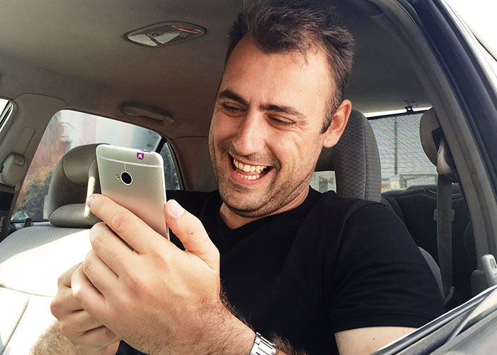 Man smiling at his phone while sitting inside a car, illustrating the impact of unexpected phone discoveries on relationships.