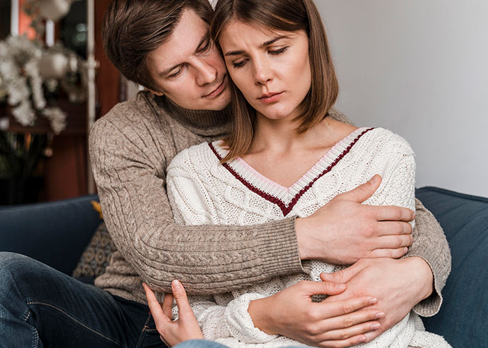 A couple sitting on a couch, looking concerned, reflecting on discoveries in their partner's phone.