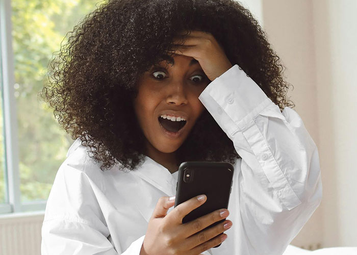 Surprised woman finding unexpected content on phone, hand on head, in disbelief.