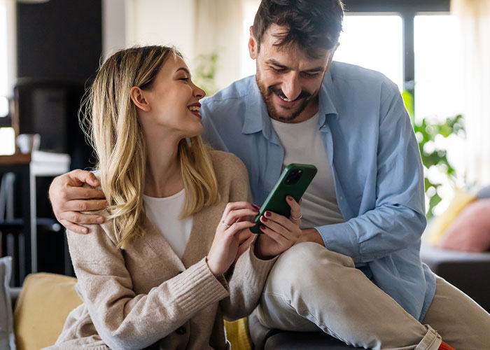 Couple smiling while looking at a phone, symbolizing discoveries that change perspectives in relationships.