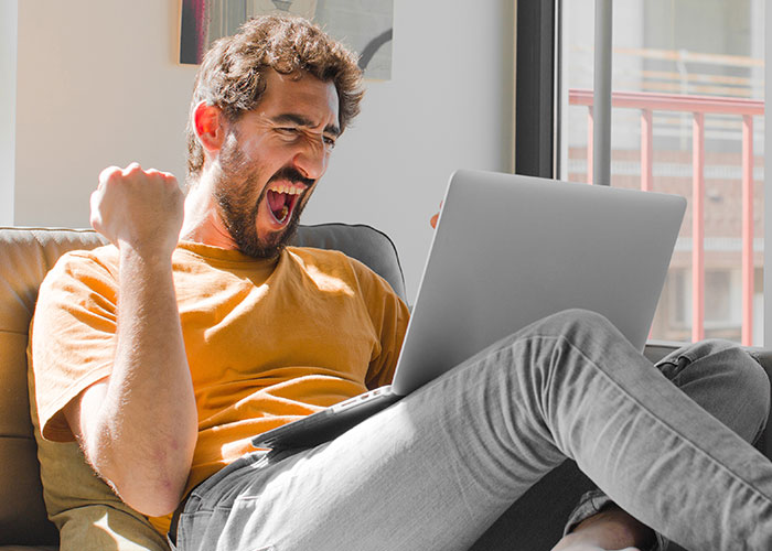 Man in a yellow shirt cheering while looking at his laptop, symbolizing reaction to unexpected phone discoveries.