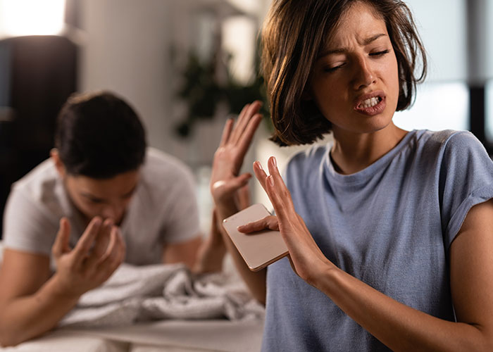 Woman upset after finding something on partner's phone, holding it while raising her hand in a defensive gesture.